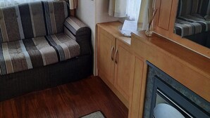 A cozy living area with a striped sofa, wooden cabinet, and a fireplace. - Beautiful 3-bed Static Caravan in Skegness (Skegness)