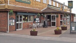 A brick building with a sign reading "HAPPY DAYS CLUB" and "ENTRANCE" visible. There are outdoor tables and chairs, and planters with plants. - Beautiful 3-bed Static Caravan in Skegness (Skegness)