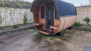 Une structure cylindrique en bois, en forme de capsule, dotée d’une porte et de bancs à l’intérieur.