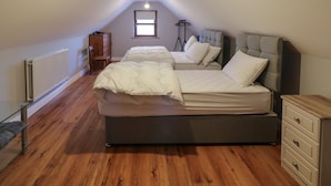 Une chambre avec deux lits, un radiateur, une commode en bois et une fenêtre.