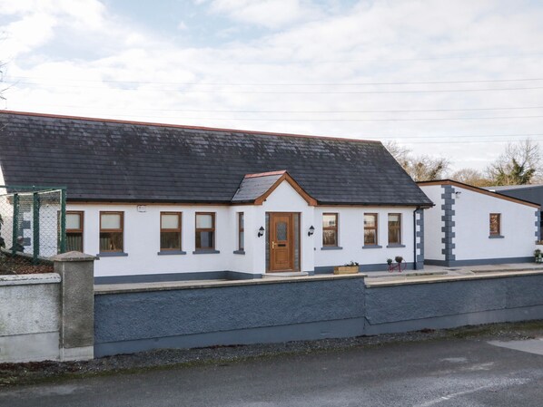 A two-story building with a grey exterior, a brown door, and multiple windows. - The Garden Cottage (Newry)