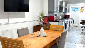 A modern kitchen with a dining area, featuring a wooden table, chairs, a TV mounted on the wall, and a red appliance. - Impeccable Spacious 6-bed House in Romford (Romford)