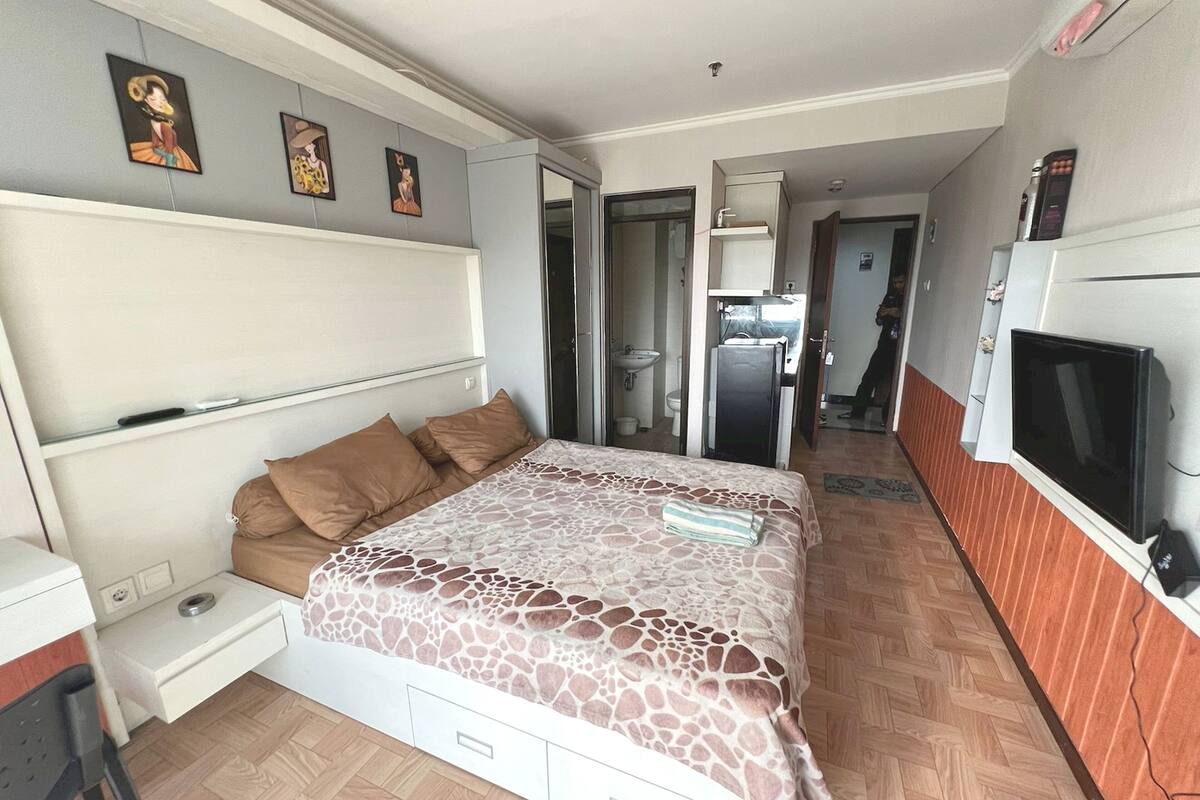 Een slaapkamer met een bed, een televisie, een bureau en een kledingkast.