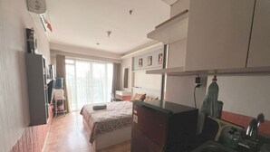 Une chambre d’hôtel compacte comprenant un lit, une petite kitchenette, un bureau et une fenêtre avec des rideaux.