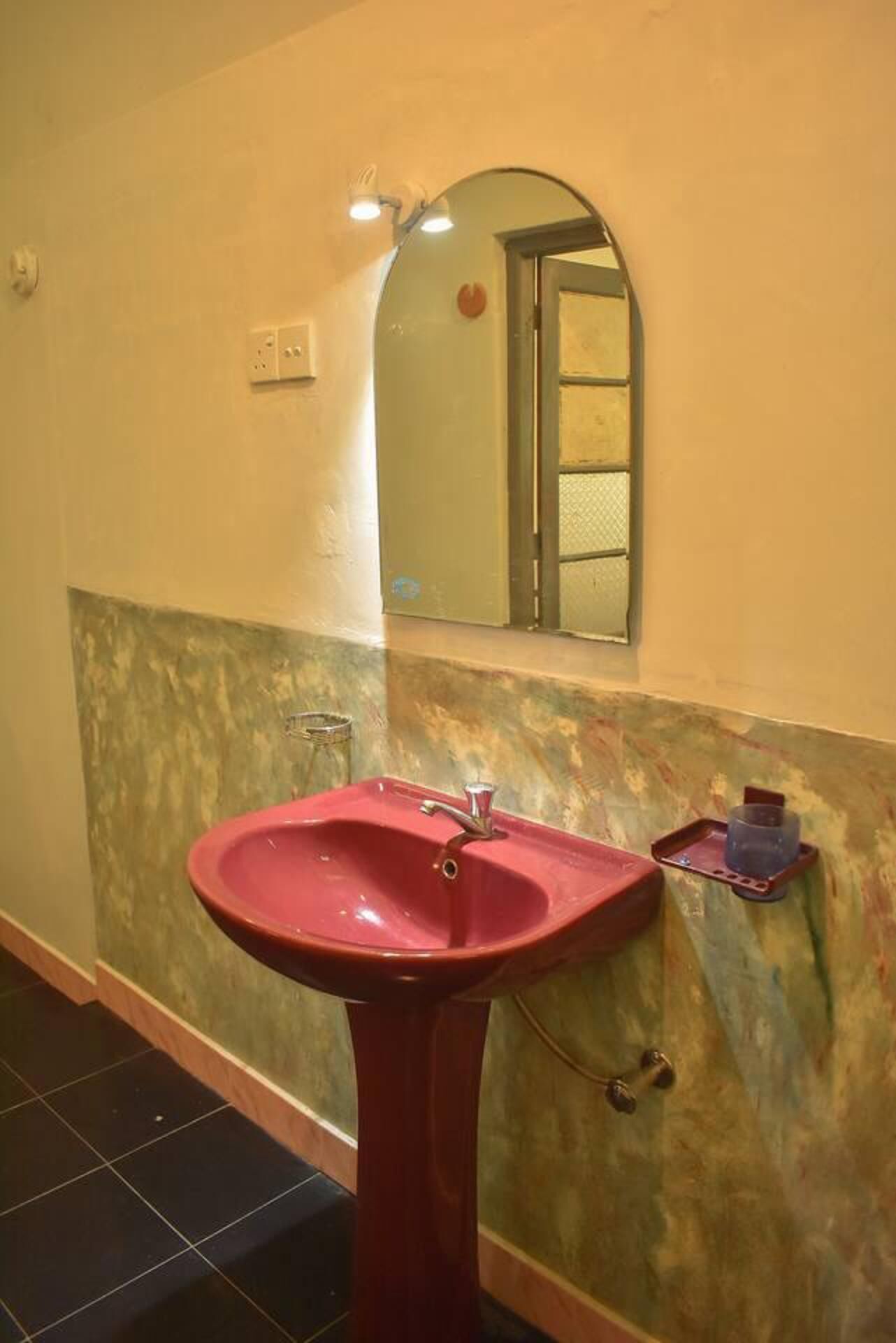 A bathroom with a red sink, a mirror, and a wall-mounted shelf.