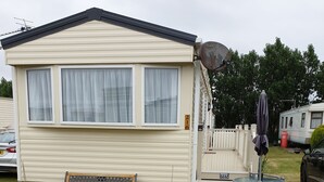 Une maison mobile dotée d’une véranda, d’un banc et d’une table avec un parasol.