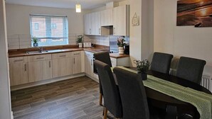 Una cucina moderna con mobili in legno, un'area pranzo con tavolo e sedie, e un'ampia finestra con tende.