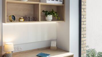 A modern study area with a wooden desk, a chair, a lamp, and shelves with plants and storage boxes.