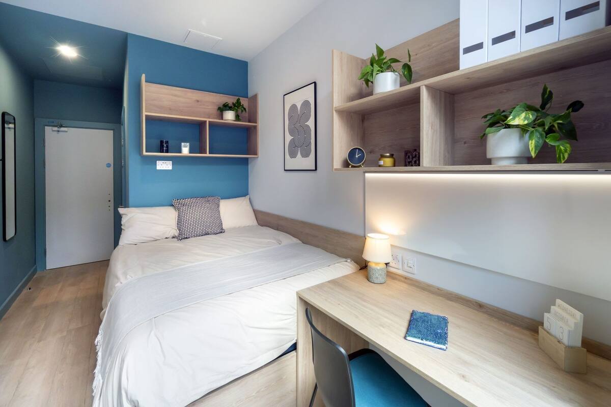 Ein modernes Schlafzimmer mit Bett, Nachttisch, Schreibtisch, Pflanzenregal und Wanduhr.