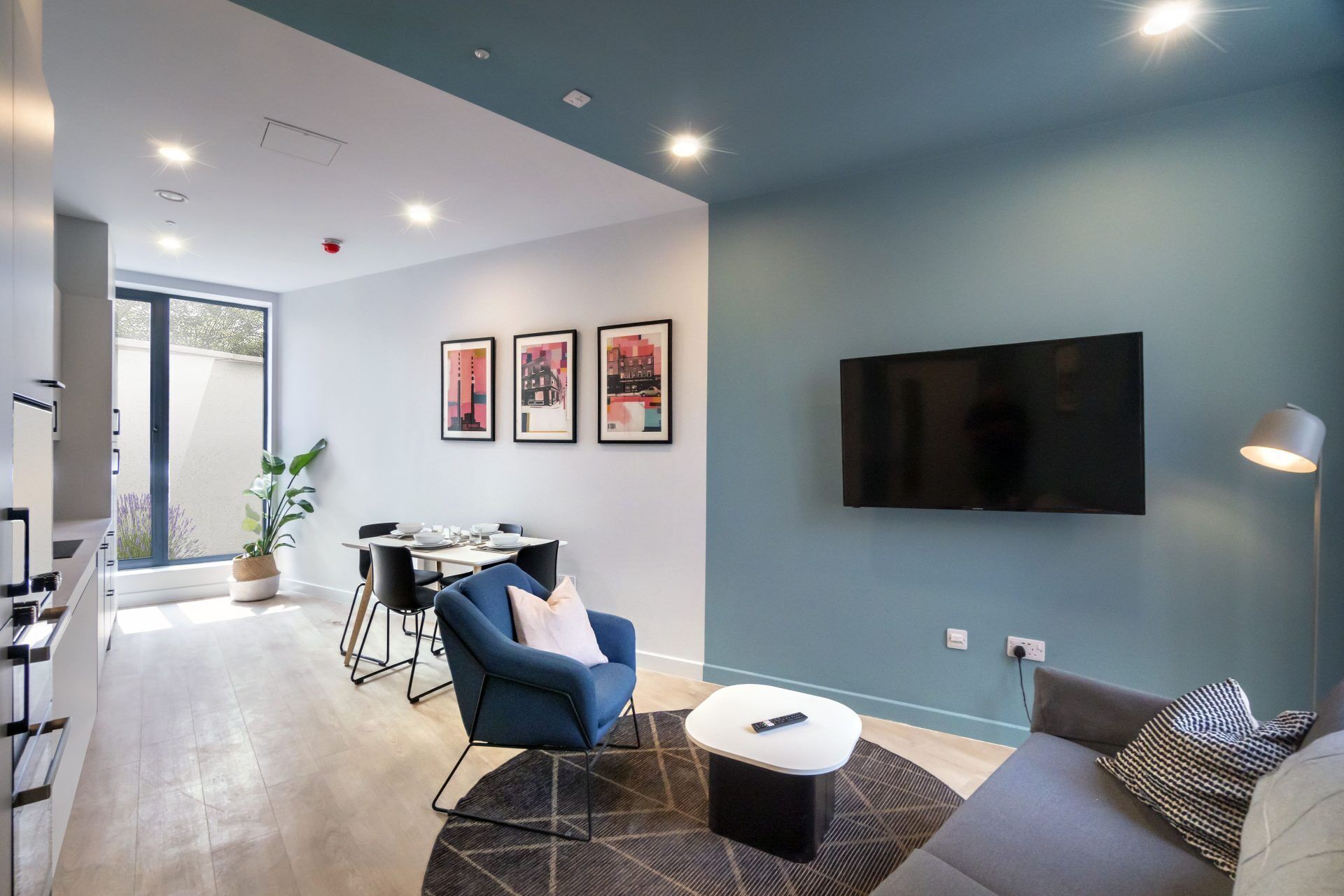 Un salon moderne comprenant un coin repas, un téléviseur à écran plat fixé au mur et une grande fenêtre laissant entrer la lumière naturelle.