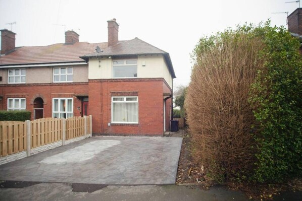 A residential property with a paved driveway, a wooden fence, and a tall shrubbery.