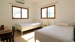 Une chambre avec deux lits simples, un bureau avec une chaise et une fenêtre donnant sur une structure verdoyante.