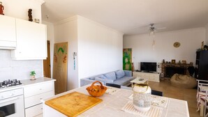 Une cuisine moderne avec des meubles blancs, une cuisinière à gaz et un plan de travail en bois. On y trouve un coin repas avec une table dressée pour deux personnes, un canapé et une cheminée.