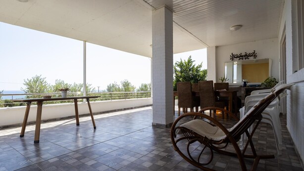 Un espace extérieur abrité, aménagé pour accueillir des clients, avec vue sur la mer, comprenant une table, des chaises et un fauteuil à bascule.
