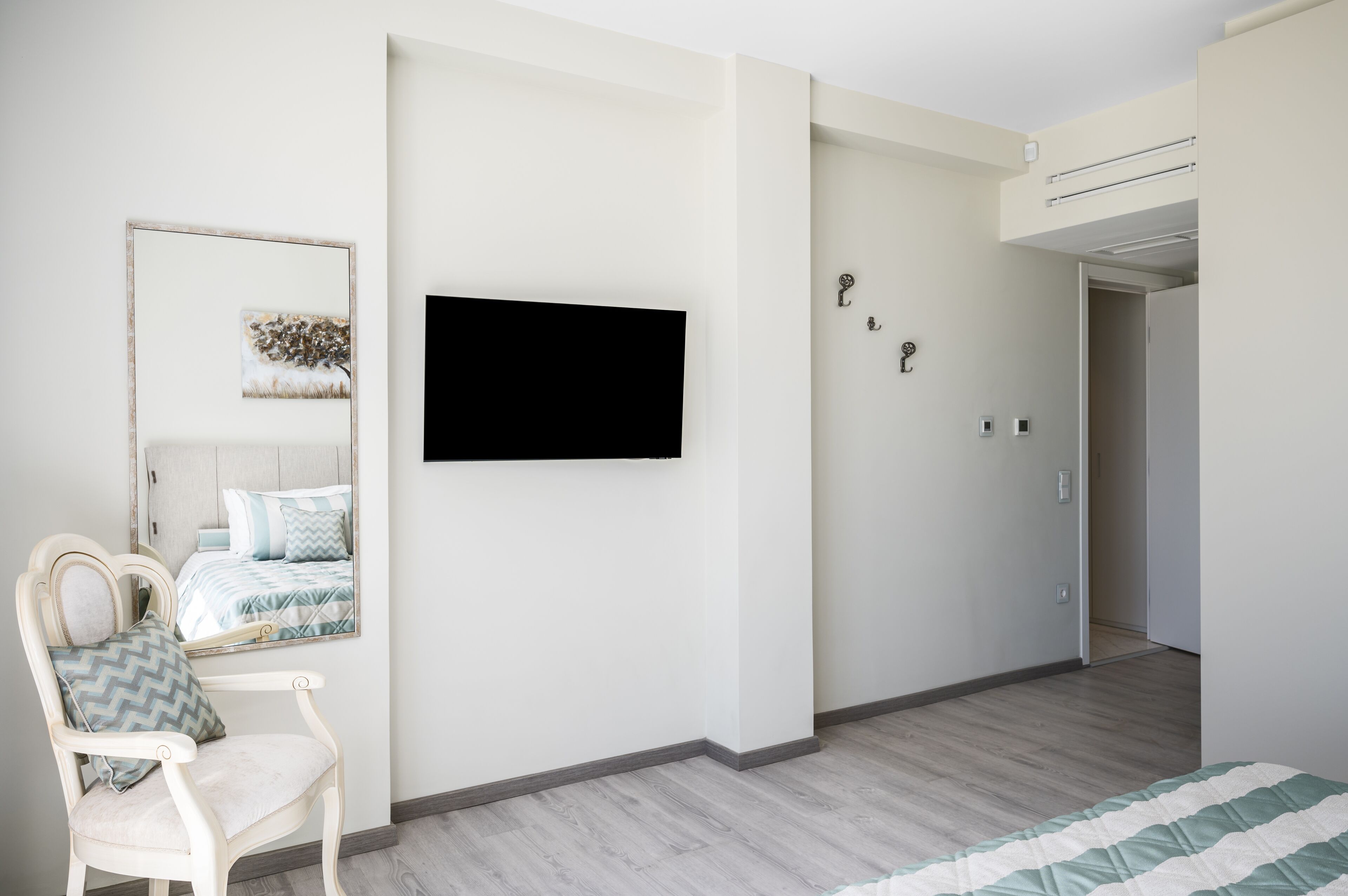 Un dormitorio con una cama, una silla, un espejo y un televisor montado en la pared.