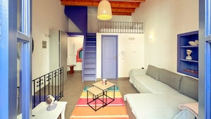 A cozy room with a wooden ceiling, a staircase, a sofa, a small table, and a colorful rug. - Kali Strata 2 - Downtown (Symi)