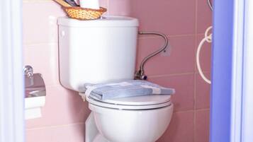 A bathroom with a toilet, a basket with a roll of toilet paper, and a shower area.