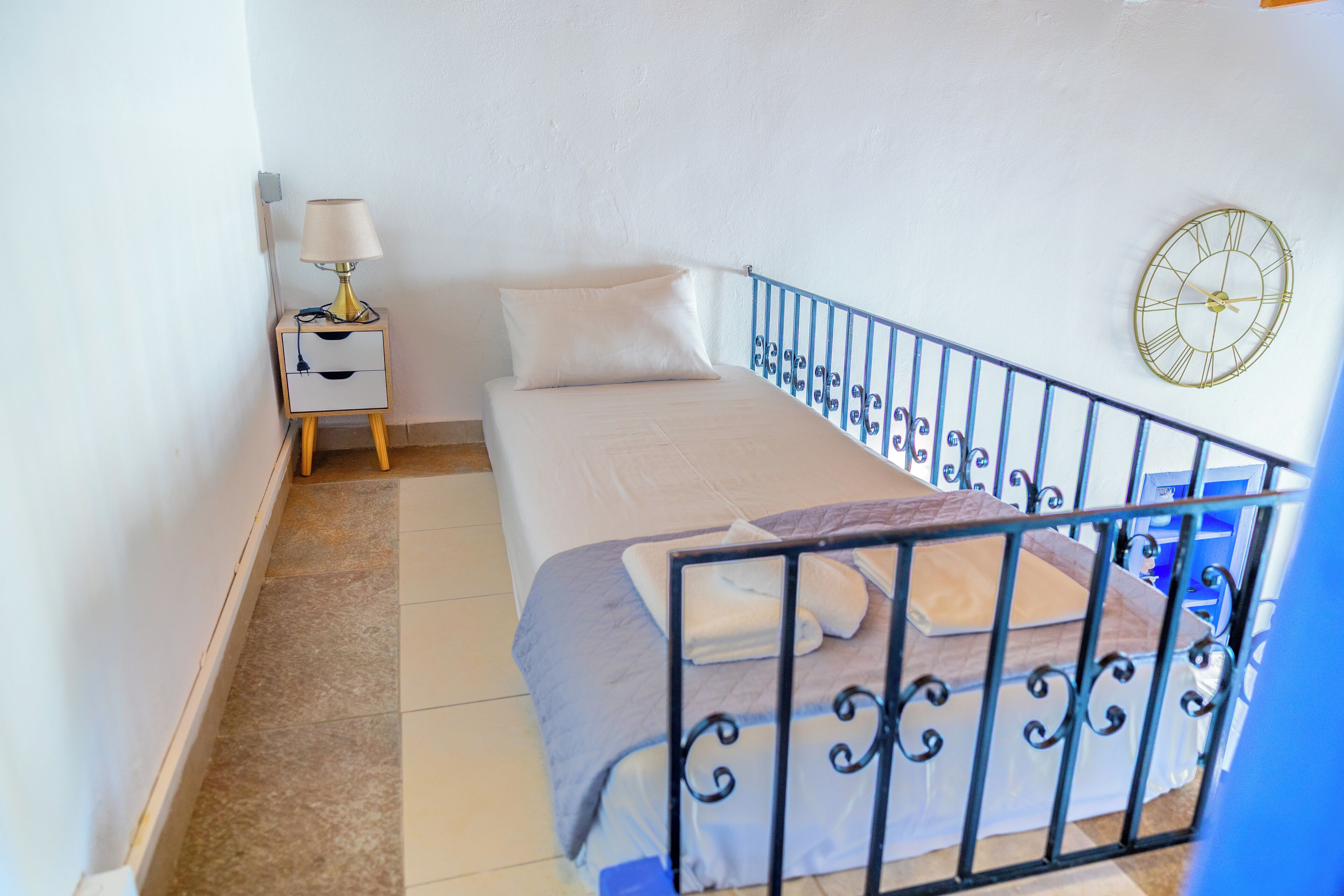 Un dormitorio con cama, mesita de noche, lámpara y reloj de pared.