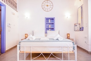 A hotel room with a bed, a wall clock, a shelf with decorative items, and a bathroom door. - Kali Strata 2 - Downtown (Symi)