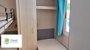 Ein kleines Zimmer mit Etagenbetten, einem Fenster mit Vorhang und einer Tür.