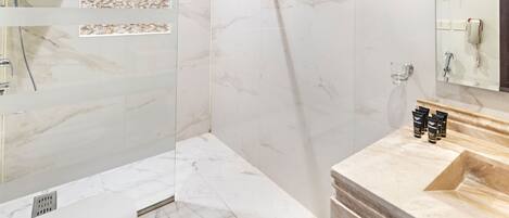 Un baño moderno con suelo de mármol, cabina de ducha con mampara de cristal, tocador con lavabo y espejo.