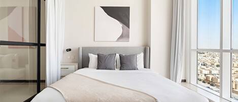 A modern bedroom with a large bed, a view of the city through floor-to-ceiling windows, and a minimalist decor.