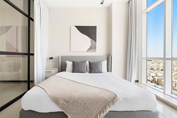 A modern bedroom with a large bed, a view of the city through floor-to-ceiling windows, and a minimalist decor. - Olaya 2 Stella Stays (Riyadh)
