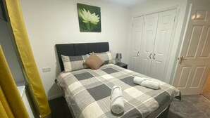 Un letto rifatto con cura, una coperta a quadri, un cuscino e due asciugamani arrotolati.