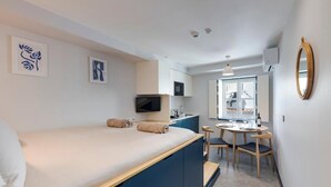 A compact hotel room with a bed, a small desk with a chair, a television, and a window. - Montain View Guesthouse Pretoria (Pretoria)