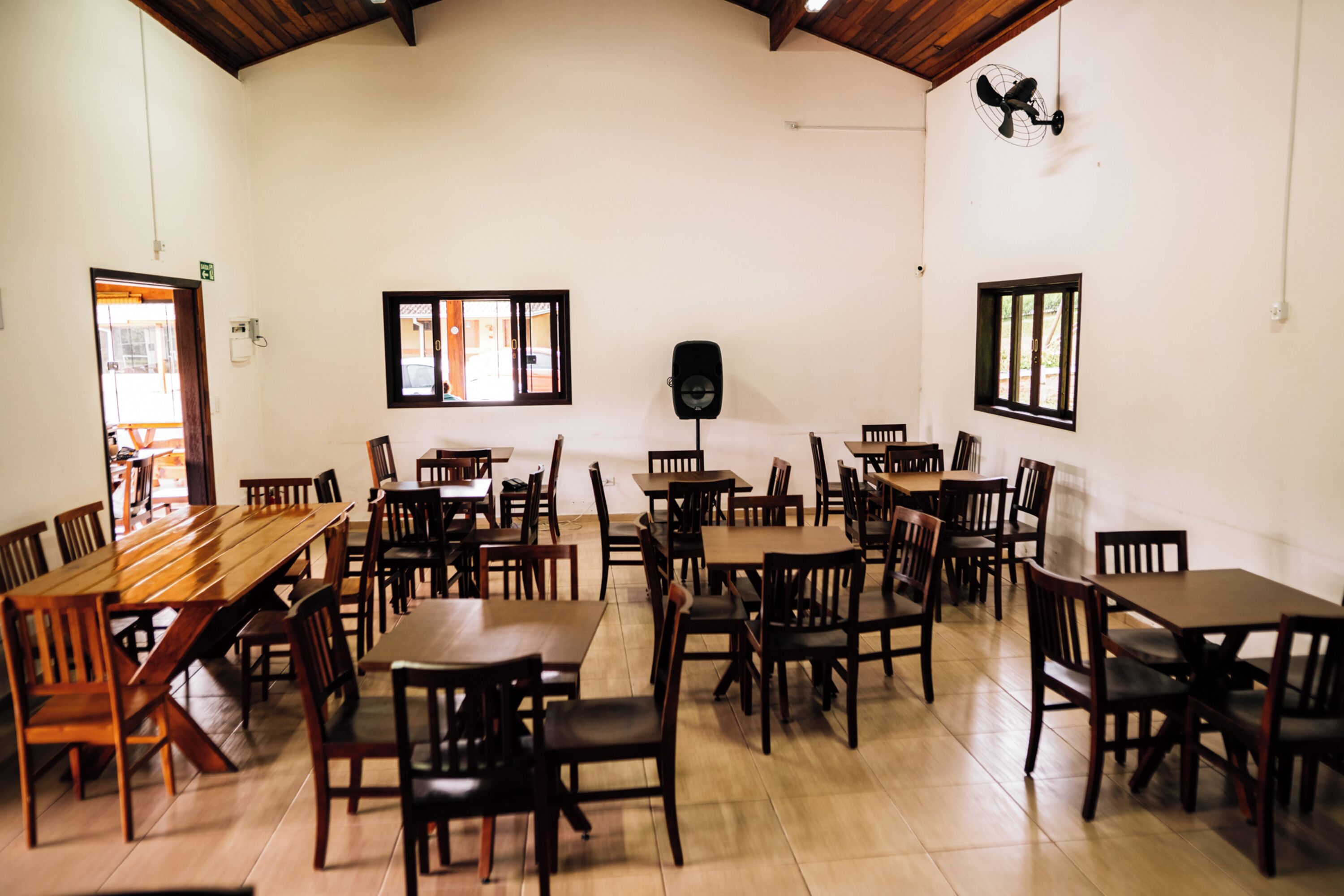 Un comedor con varias mesas y sillas de madera, un ventilador de techo y una ventana con persianas.