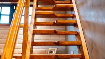 A wooden staircase with a handrail, leading up to a landing with a white wall and a window.