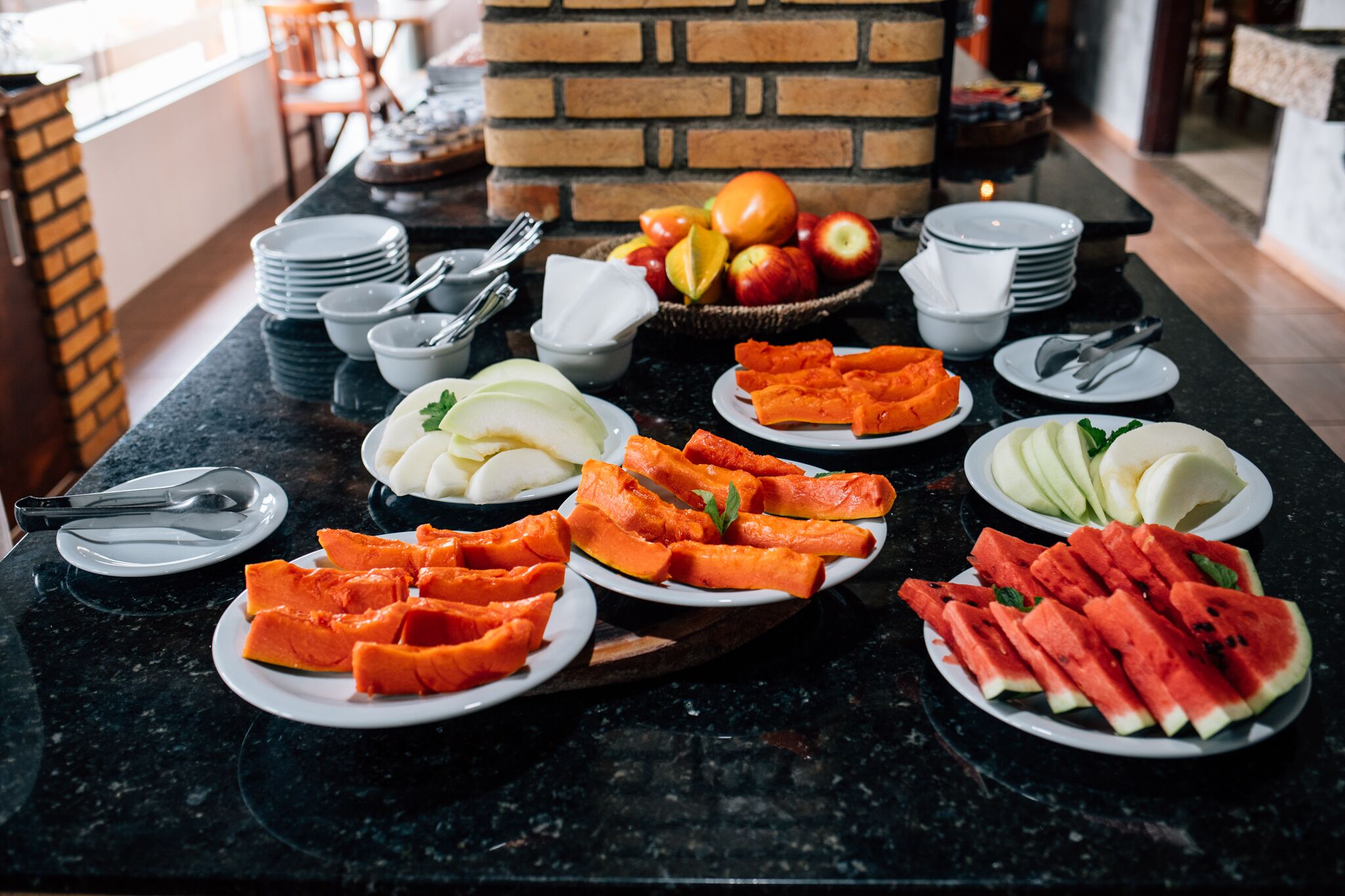 A breakfast buffet with various fruits and vegetables on a marble countertop.