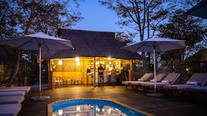 A poolside area with lounge chairs, umbrellas, and a bar area with seating. - Mankwe Tented Retreat (Maun)