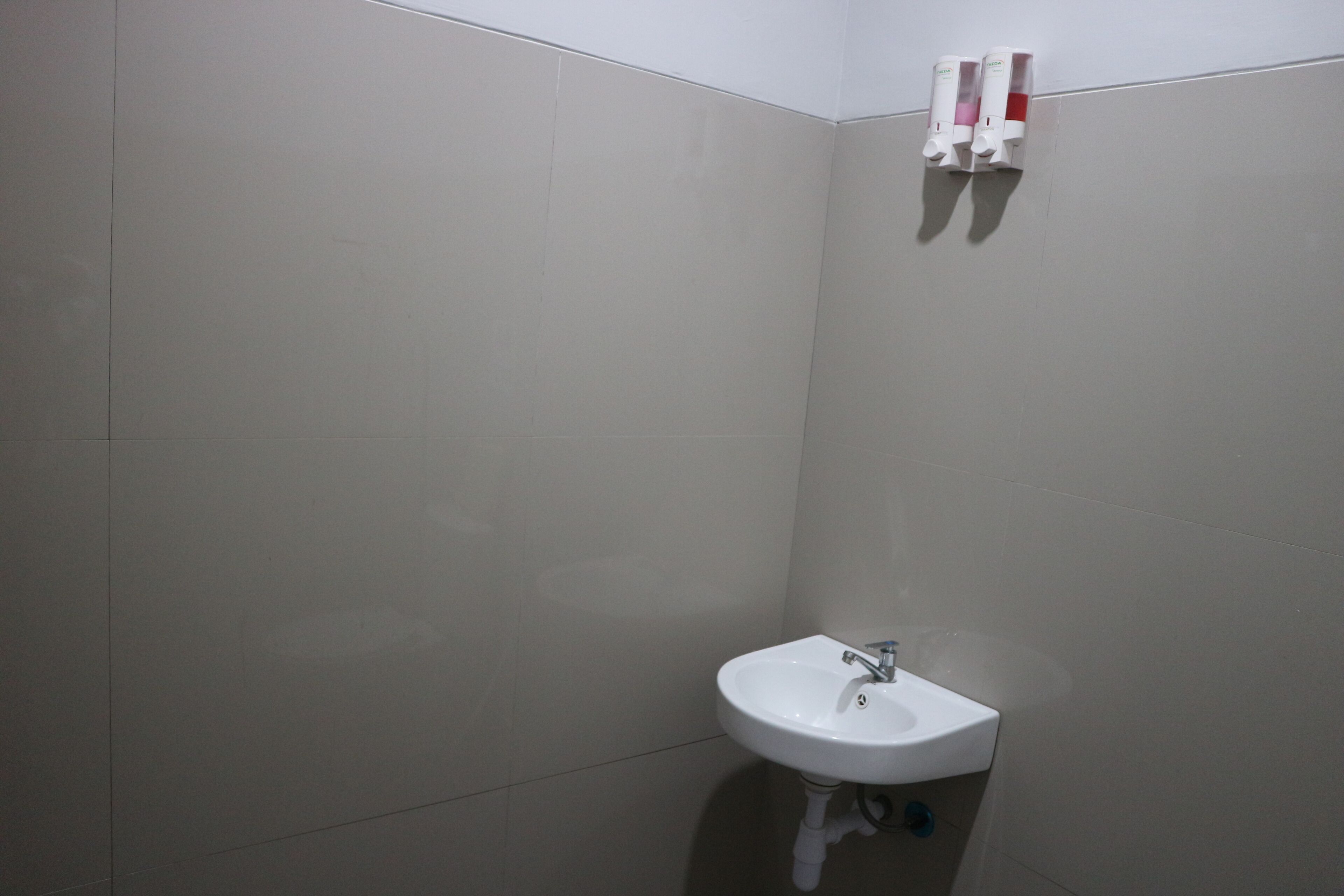 A bathroom with a white sink, a mirror, and two hand soap dispensers mounted on the wall.