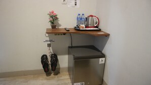 A compact kitchenette with a refrigerator, a coffee maker, bottled water, and a small potted plant. - K1 UPN (Surabaya)