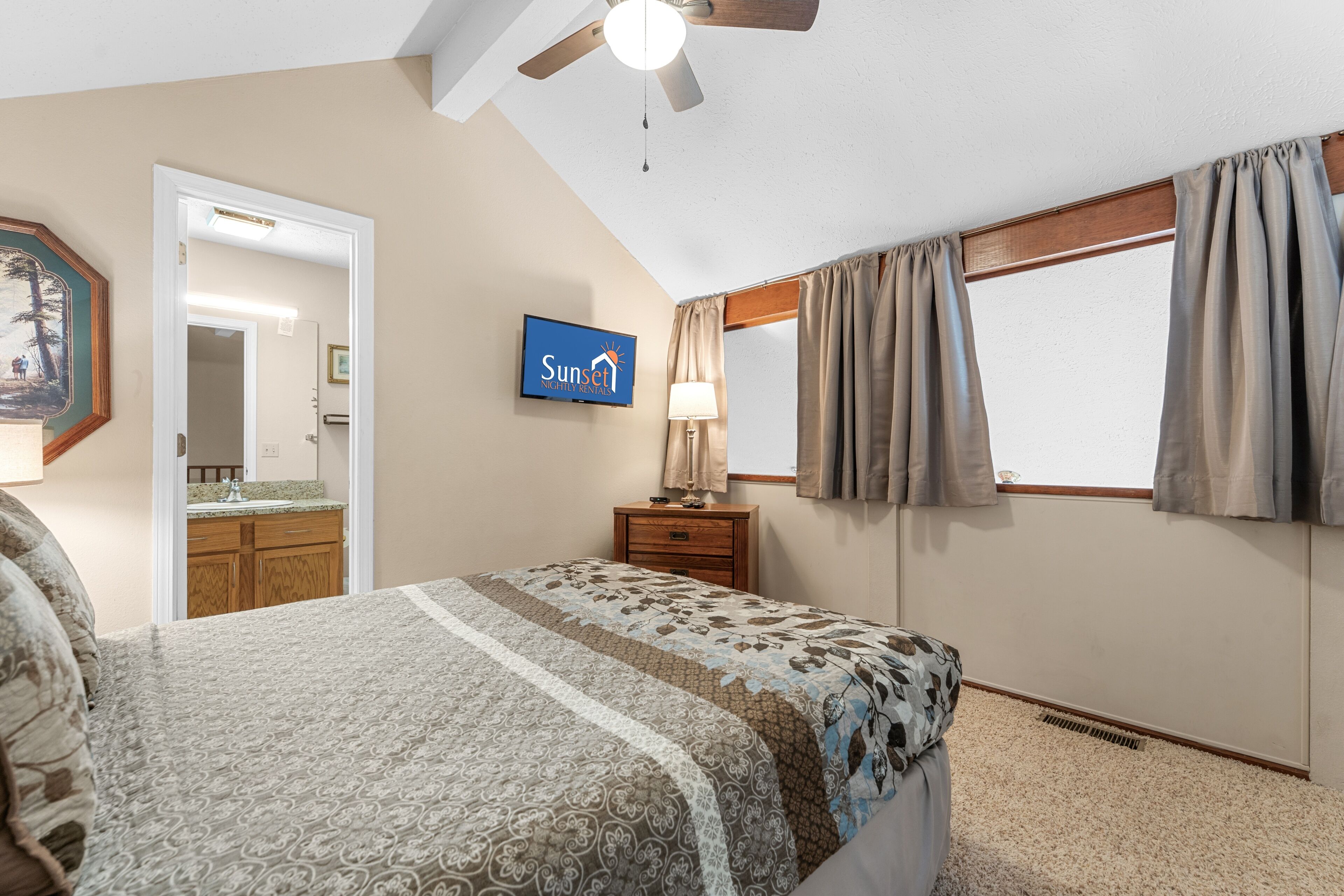 A bedroom with a bed, a nightstand, a television, and a window with curtains.