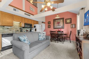 A living room with a gray sofa, wooden cabinets, a kitchen with a stone backsplash, and a dining area with a table and chairs. - Dreamers Delight 2 Bedroom Condo by RedAwning (Branson)