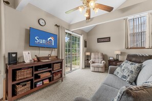 A living room with a television, a ceiling fan, a sofa, a chair, and a window with curtains. - Dreamers Delight 2 Bedroom Condo by RedAwning (Branson)