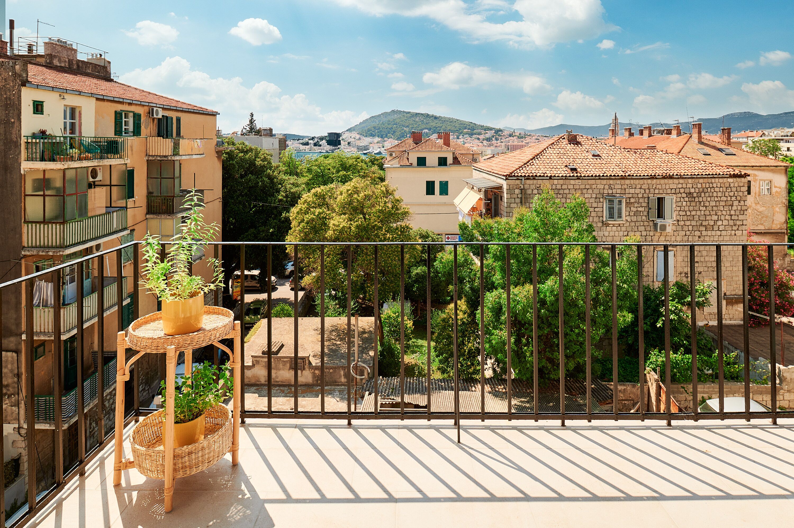A balcony with a wicker plant stand and a view of a cityscape with buildings and trees.