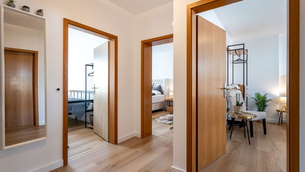 Un interior moderno con suelo de madera, una zona de comedor con mesa y sillas, y un dormitorio con cama y mesita de noche.