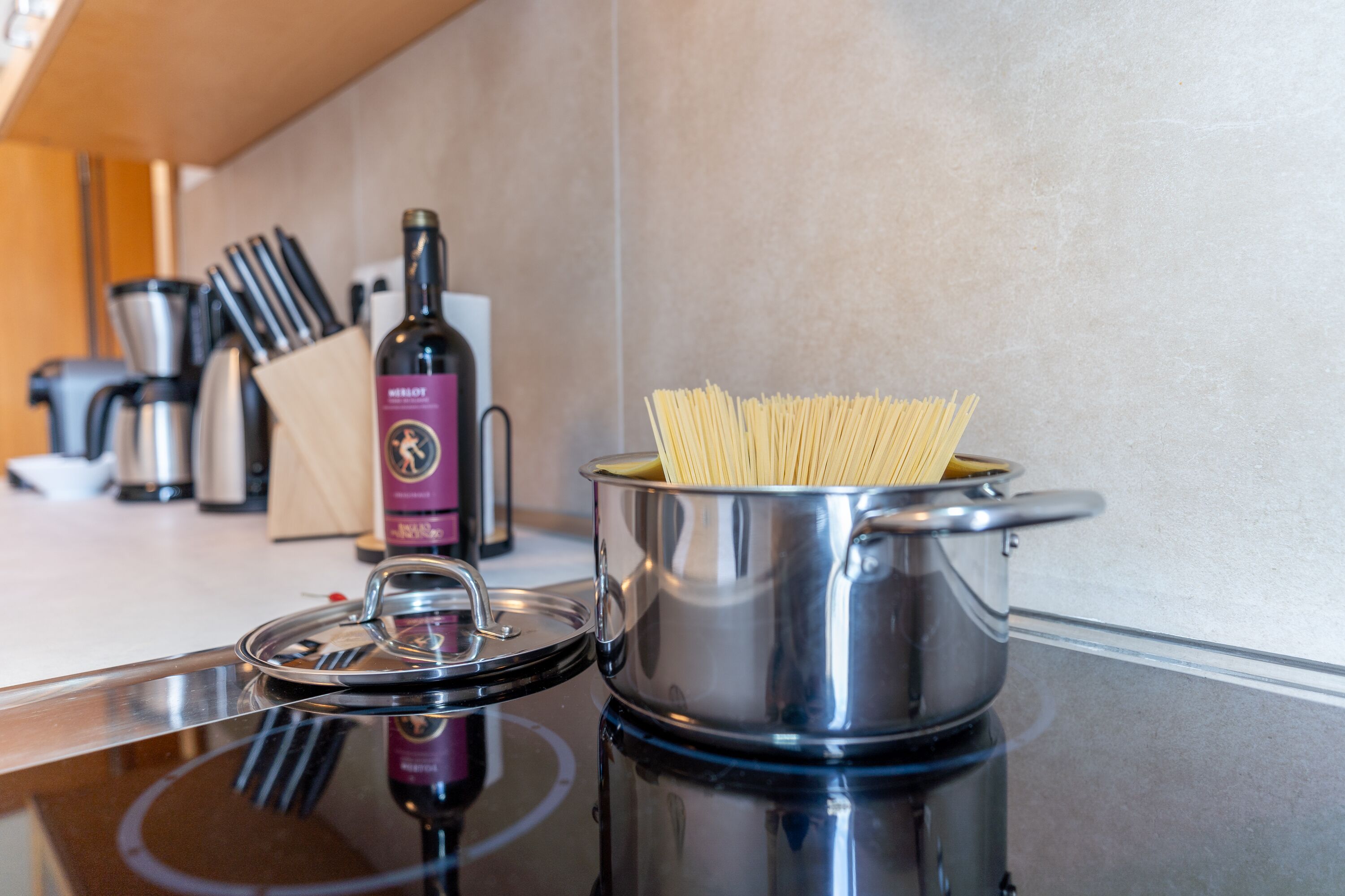 Una cocina con una olla de espagueti, una botella de vino y varios utensilios de cocina.