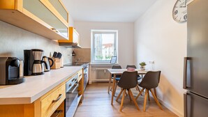 Una cocina moderna con armarios de madera, horno empotrado, cafetera y comedor con mesa y sillas.