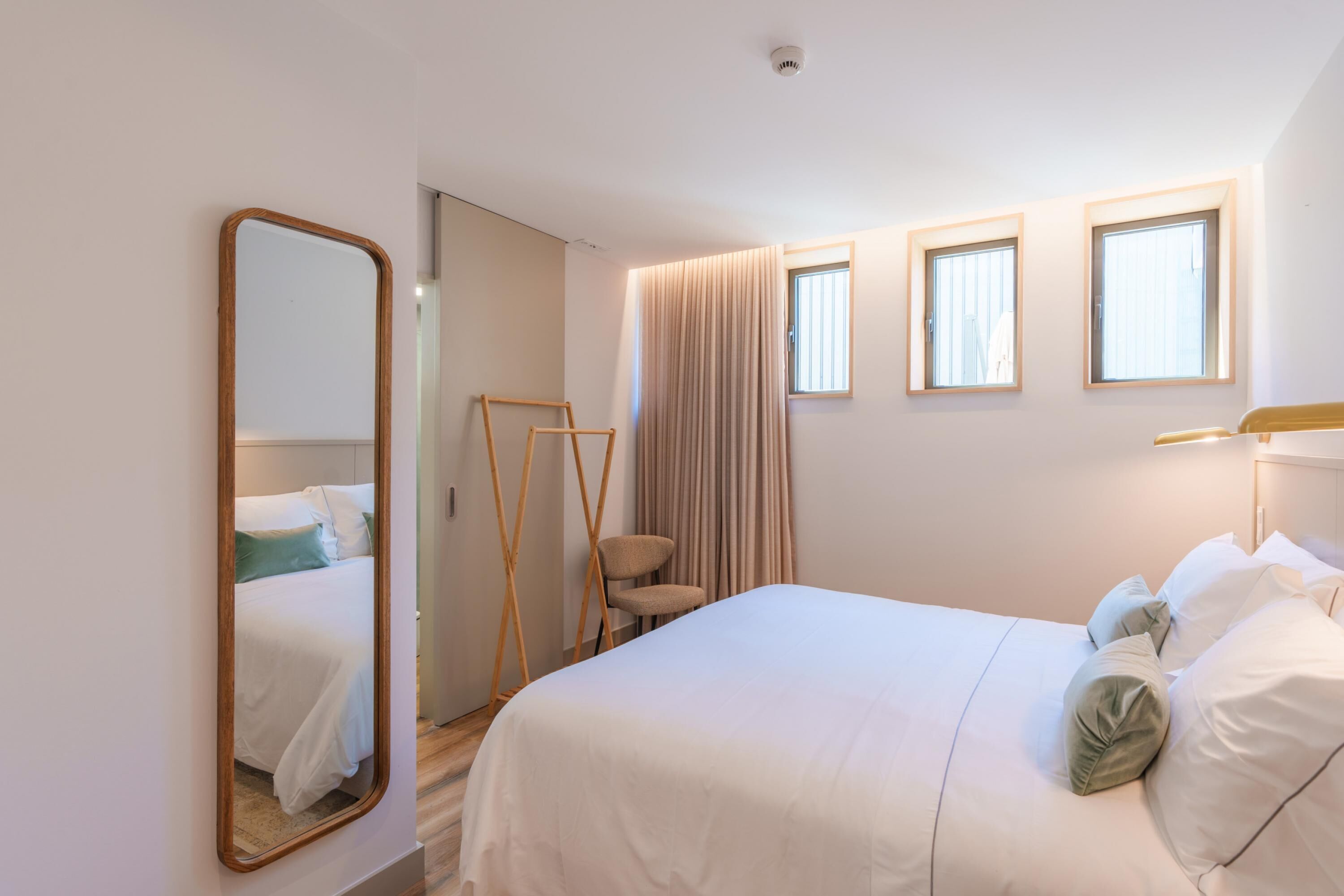 Um quarto com uma cama, um espelho, uma janela e uma cadeira.