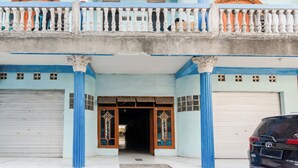 A building with a balcony, two garage doors, and a car parked in front. - Hotel O Triple N Homestay (Sidoarjo)