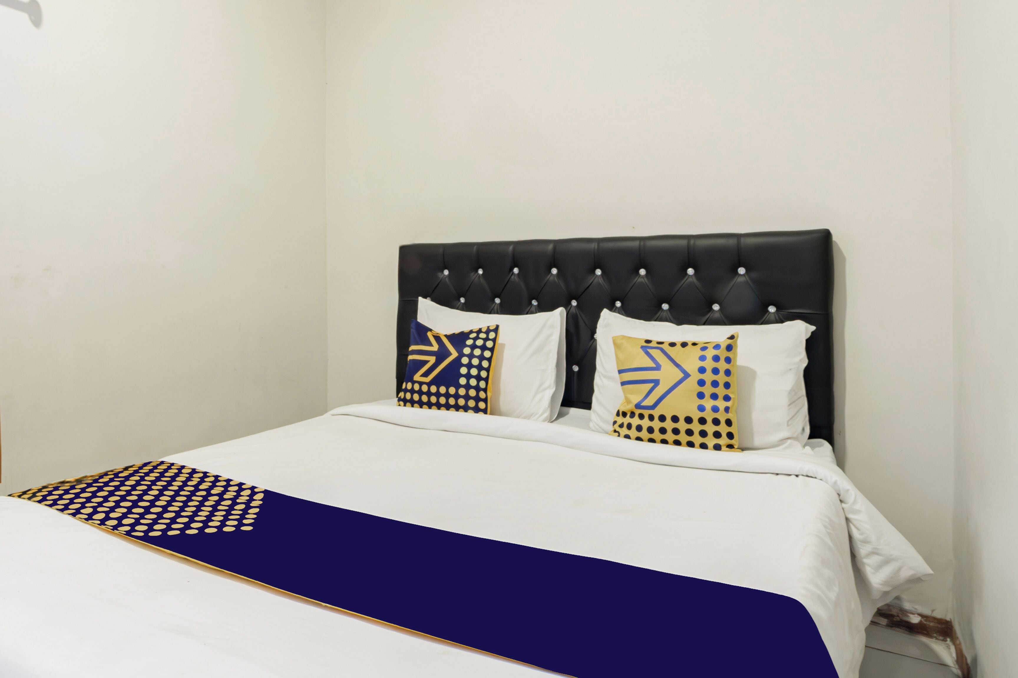 Un lit avec une tête de lit noire, une literie blanche et deux coussins décoratifs aux motifs géométriques.
