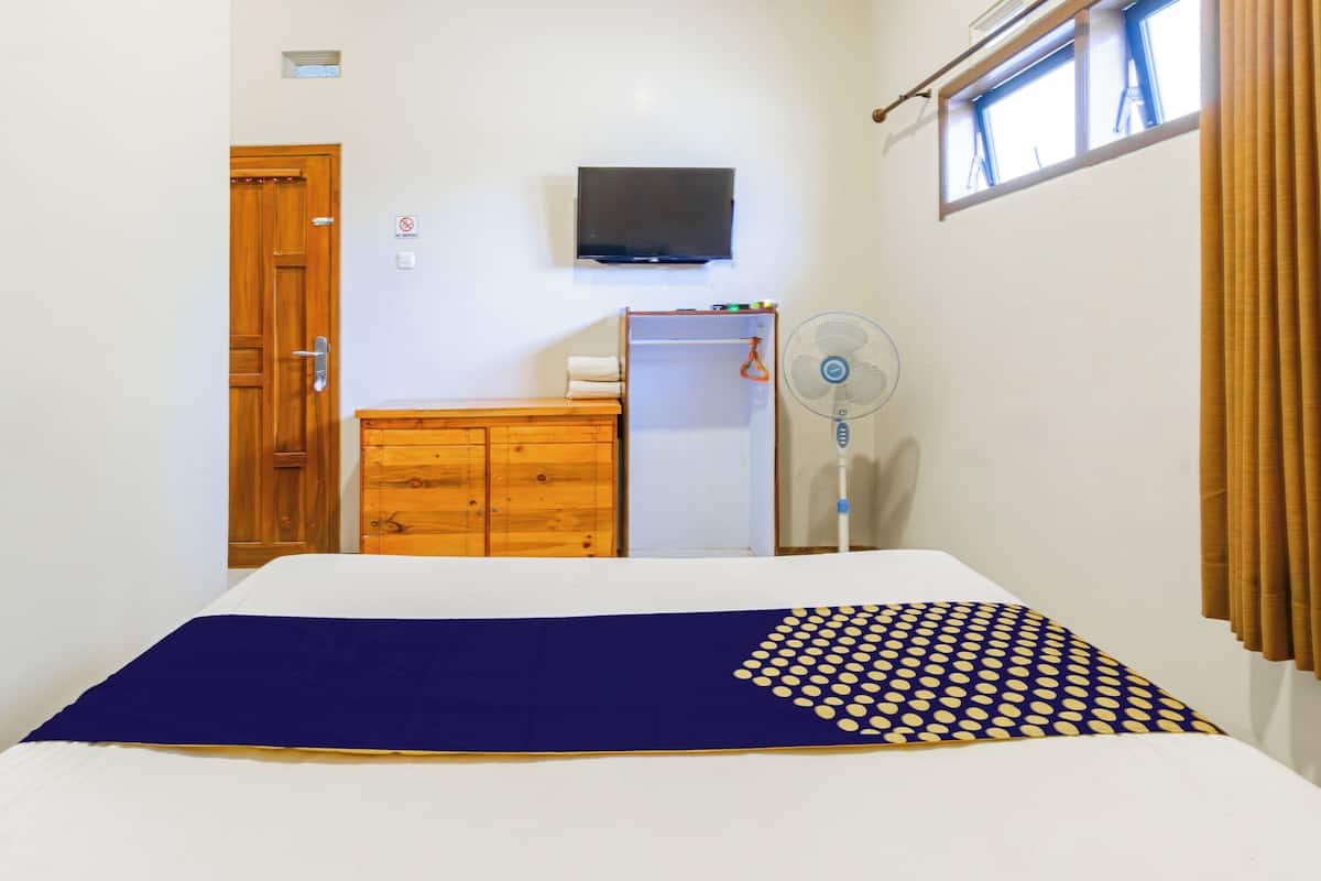 Un dormitorio con cama, cómoda de madera, televisor y ventana con cortinas.
