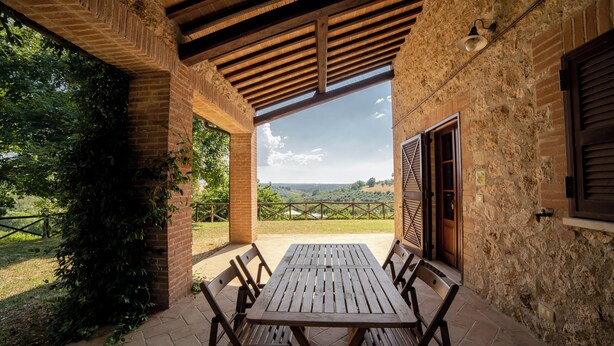 An outdoor patio with a wooden table and chairs, surrounded by stone walls and a view of the countryside. - Scappo in Umbria, Dolce Godera (LUGNANO IN TEVERINA)