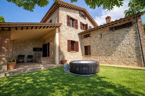 A stone house with a covered patio, outdoor seating, and a hot tub.
