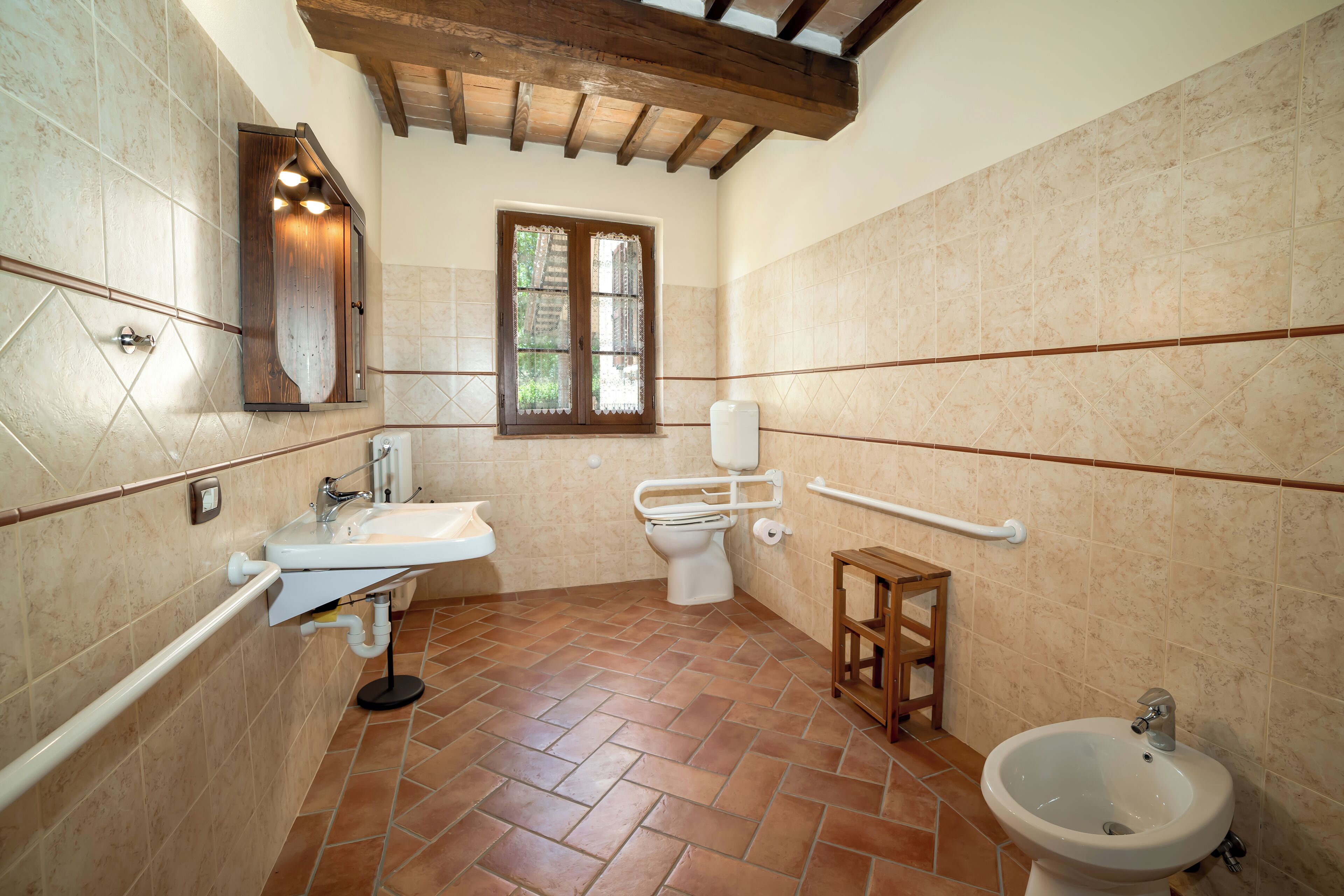 Ein Badezimmer mit Waschbecken, Toilette, Bidet und einem kleinen Holzschemel.