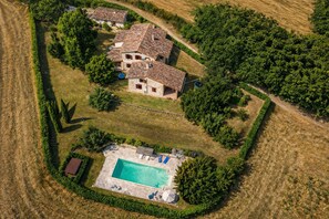 An aerial view of a property with a swimming pool, a stone house, and surrounding greenery.